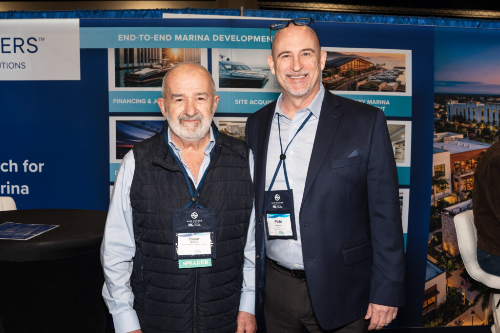 Two men standing side by side at a trade show, engaged in conversation and surrounded by various exhibition displays.