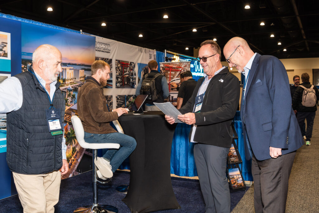 Three men engaged in conversation at a trade show booth, discussing products and networking with attendees.
