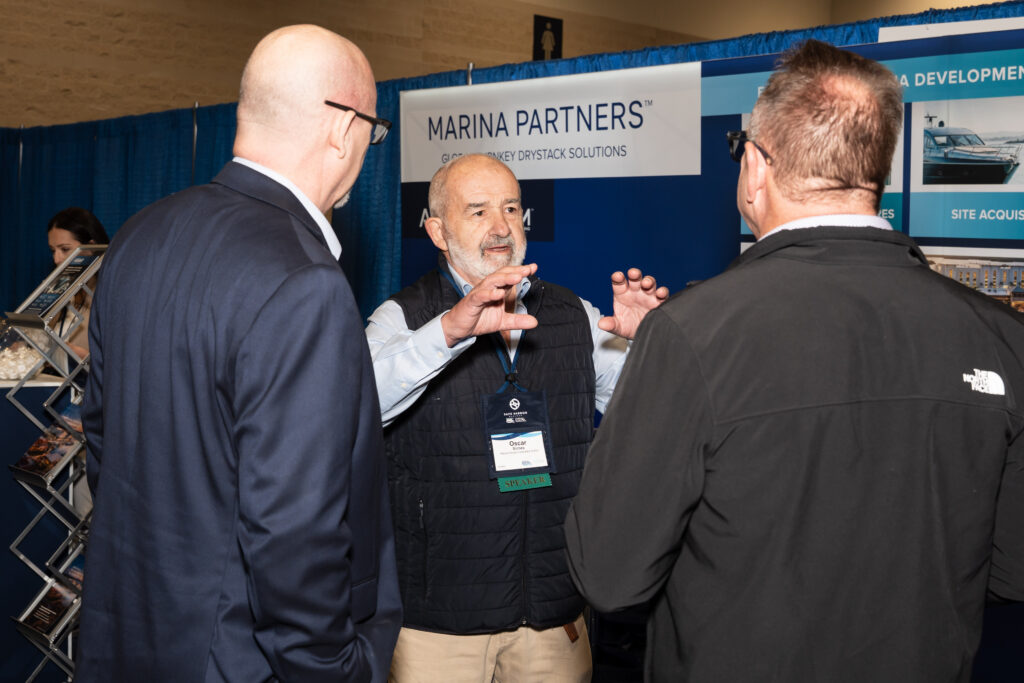 Three men engaged in conversation at a trade show booth, discussing products and networking with attendees.