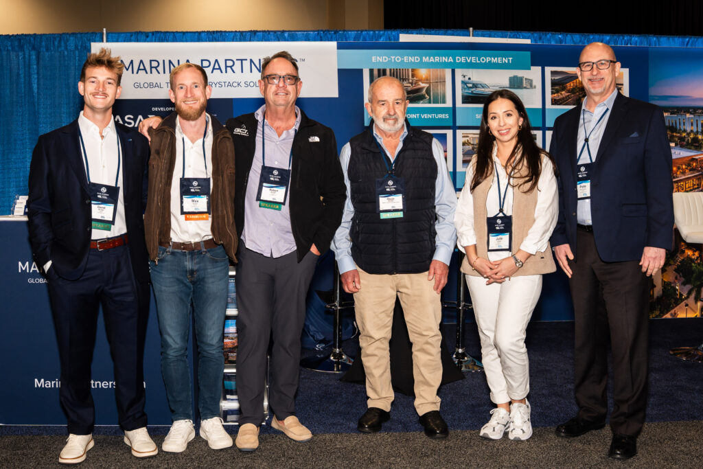 A diverse group of people gathered in front of a booth, engaging in conversation and looking at displayed materials.