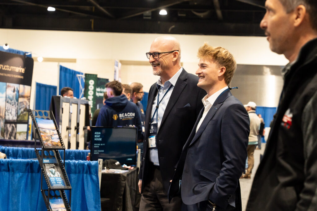 Two men standing side by side at an exhibit, engaged in conversation and observing the displayed items.