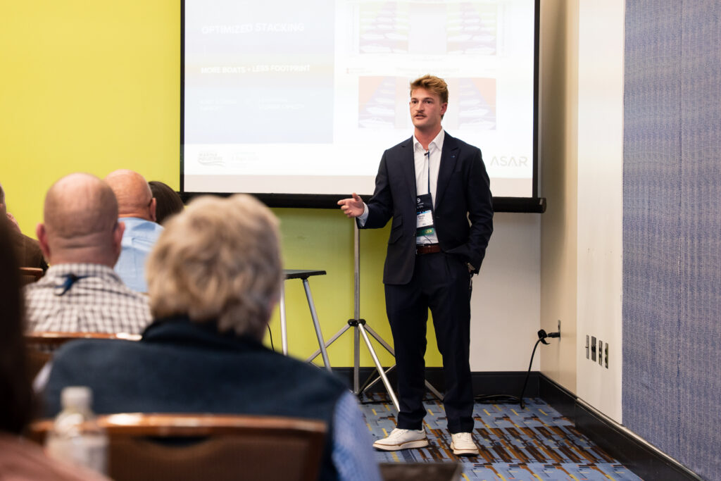 A man in a suit presents to an audience, engaging them with his speech and visual aids.