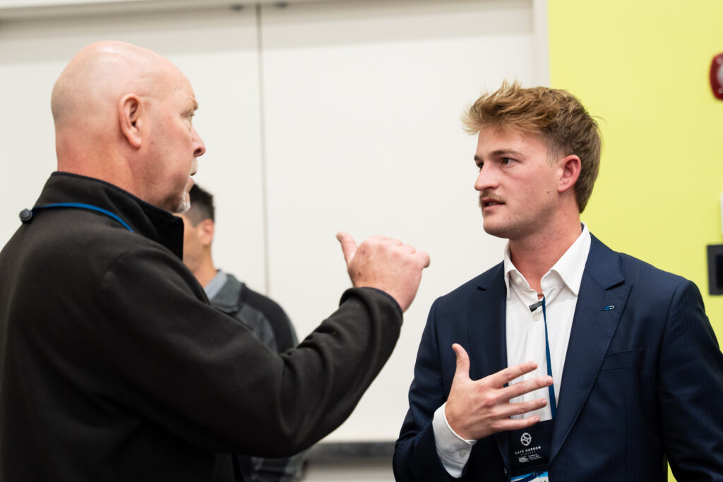 Two men discussing in a room featuring a simple white wall.