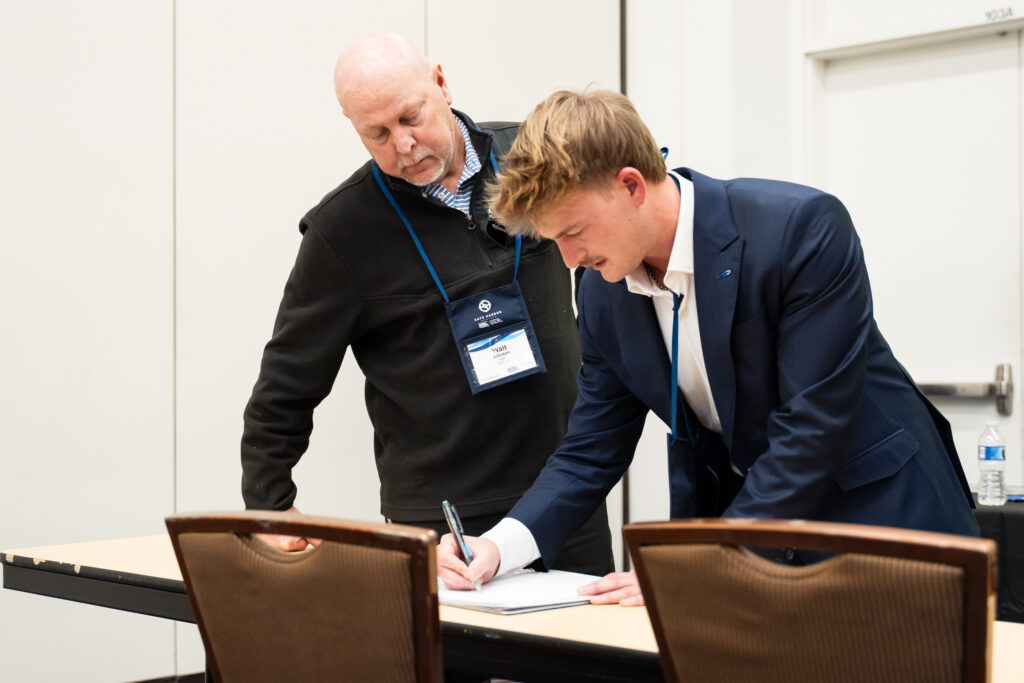 Two men are signing documents at a conference table, engaged in a formal discussion.