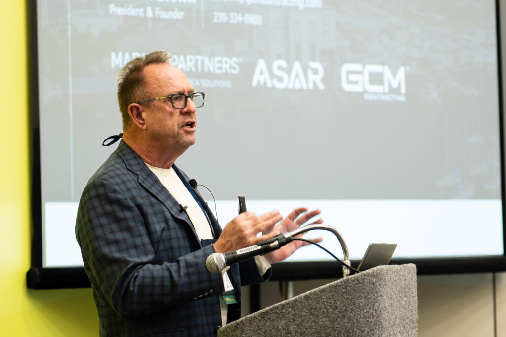 A man wearing glasses delivers a presentation at a conference, engaging the audience with his speech.