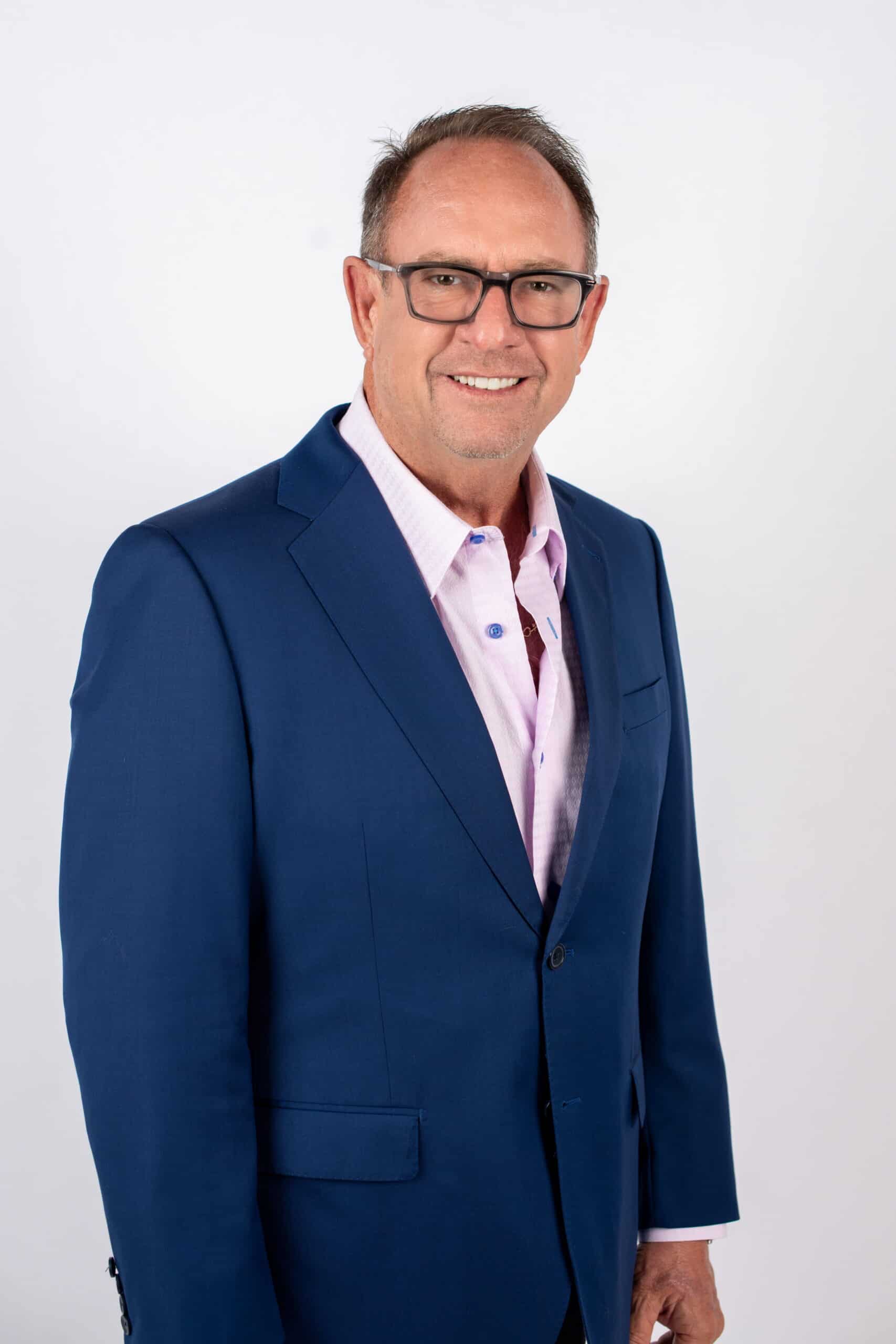 A man wearing a blue suit and glasses stands confidently, showcasing a professional appearance.