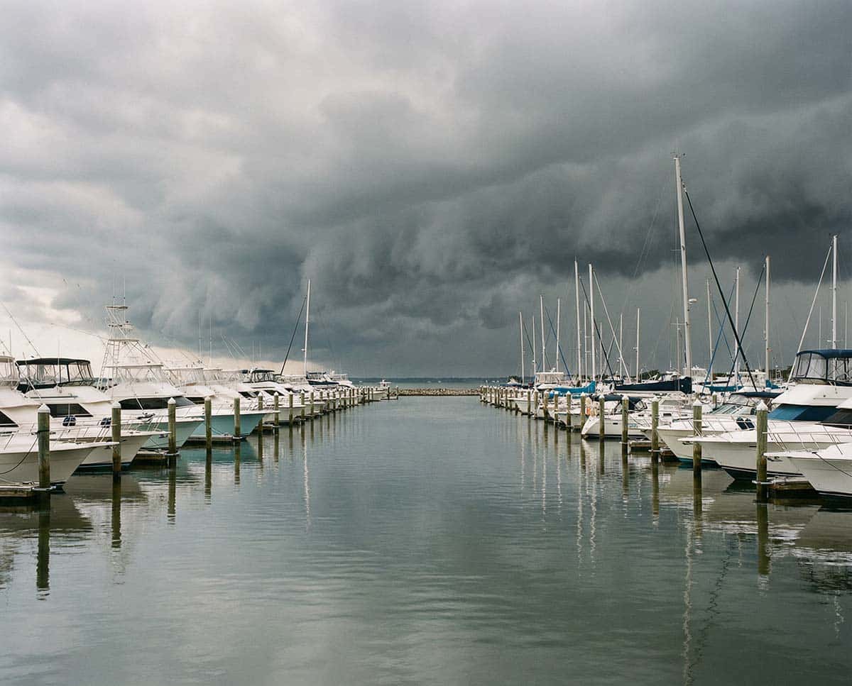 Dark storm clouds gather ominously over a marina filled with boats, signaling an approaching storm.