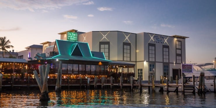 The marina restaurant silhouetted against a vibrant sunset, reflecting warm hues on the water's surface.